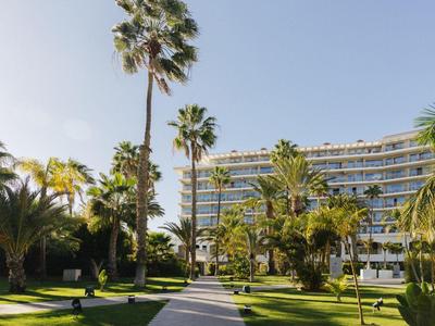 Complesso alberghiero moderno con palme e giardino curato sotto un cielo limpido.