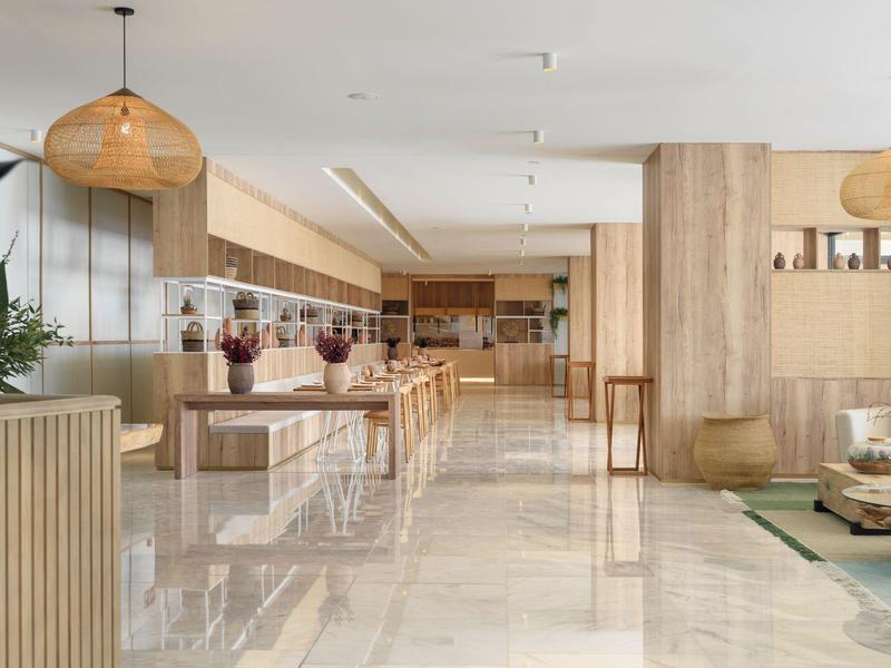 Luminoso atrio moderno di hotel con rivestimenti in legno, aree salotto e lampade sospese.