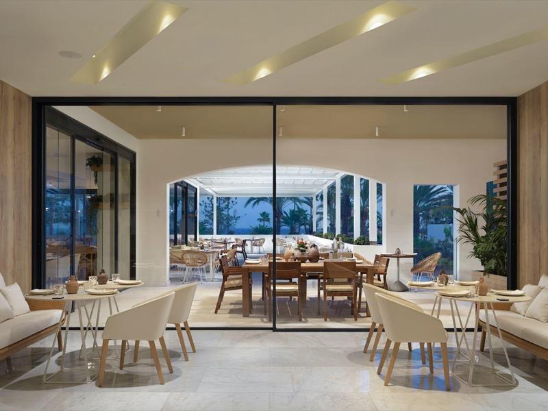 Ristorante moderno con mobili in legno chiaro e grandi finestre di vetro con vista sul mare.