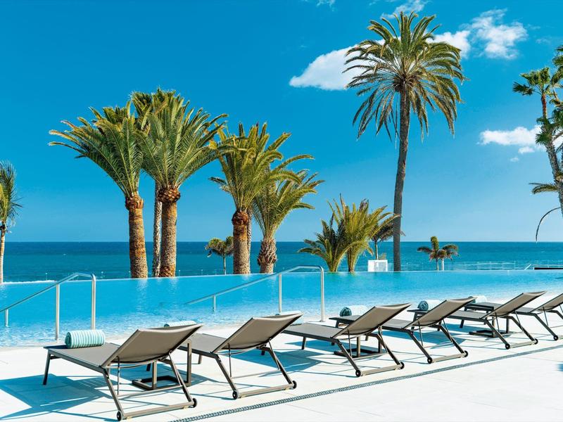 Area piscina con lettini e palme vista mare e cielo azzurro