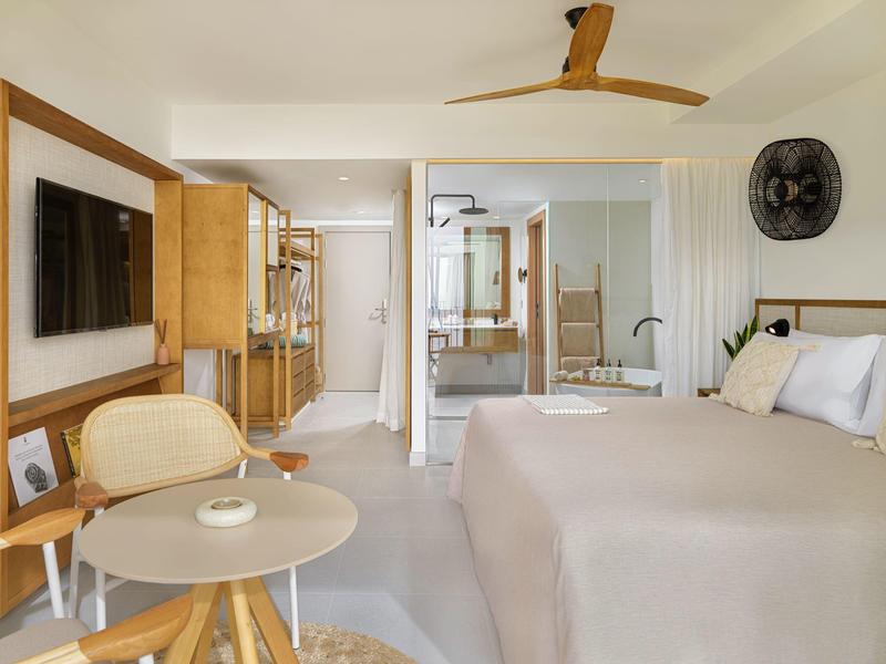 Camera d'hotel moderna con letto, TV, area salotto e bagno sullo sfondo.