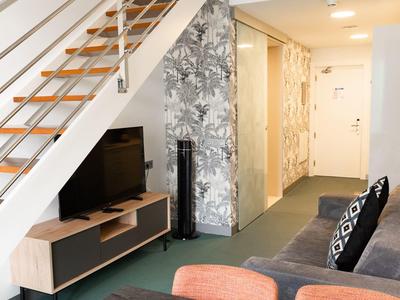 Interno moderno di camera d'hotel con scala, TV, divano e piante decorative.