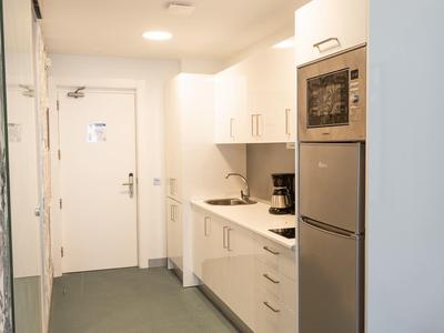 Area cucina moderna nel corridoio della camera d'hotel con armadietti bianchi e elettrodomestici.