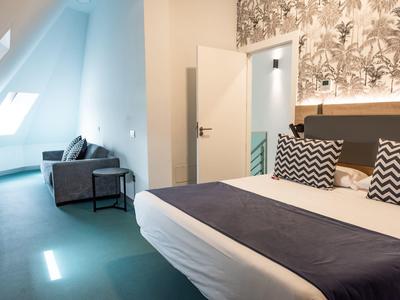 Camera moderna con letto matrimoniale, cuscini decorativi e divano vicino alla finestra.