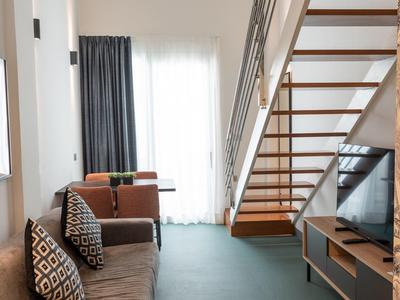 Soggiorno luminoso con divano, scala e grande finestra con tende.