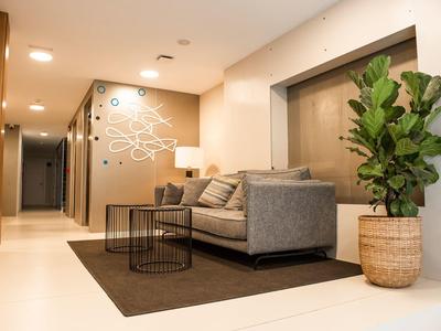 Moderner Wartebereich mit grauer Couch, schwarzen Tischen, braunem Teppich und großem grünen Pflanzenkorb.