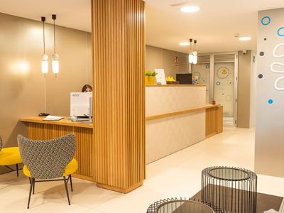 Reception di hotel moderna con elementi in legno chiaro, area salotto e arredamento minimalista.