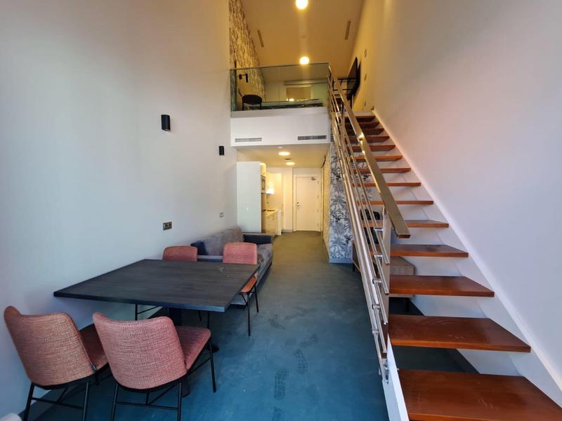 Interno moderno con moquette blu, tavolo da pranzo e scala aperta verso il piano superiore.