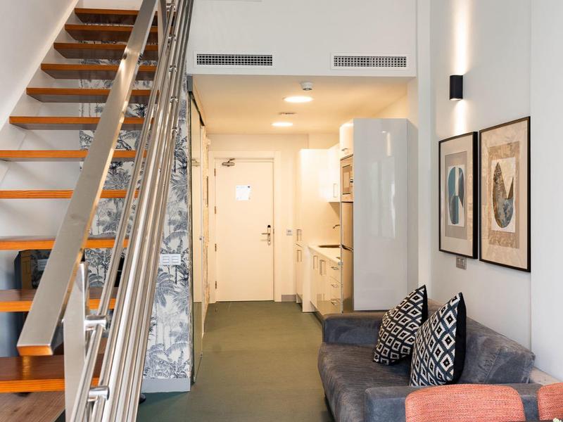 Corridoio in appartamento moderno con scala, divano, frigorifero e cuscini colorati.