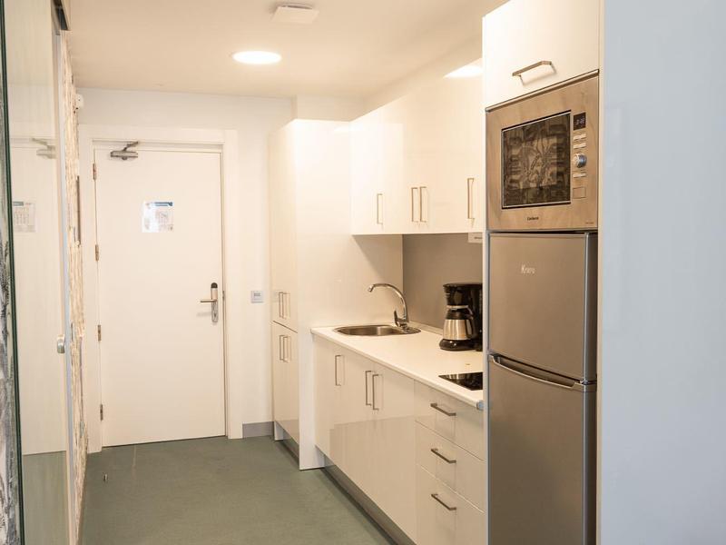 Area cucina moderna nel corridoio della camera d'hotel con armadietti bianchi e elettrodomestici.