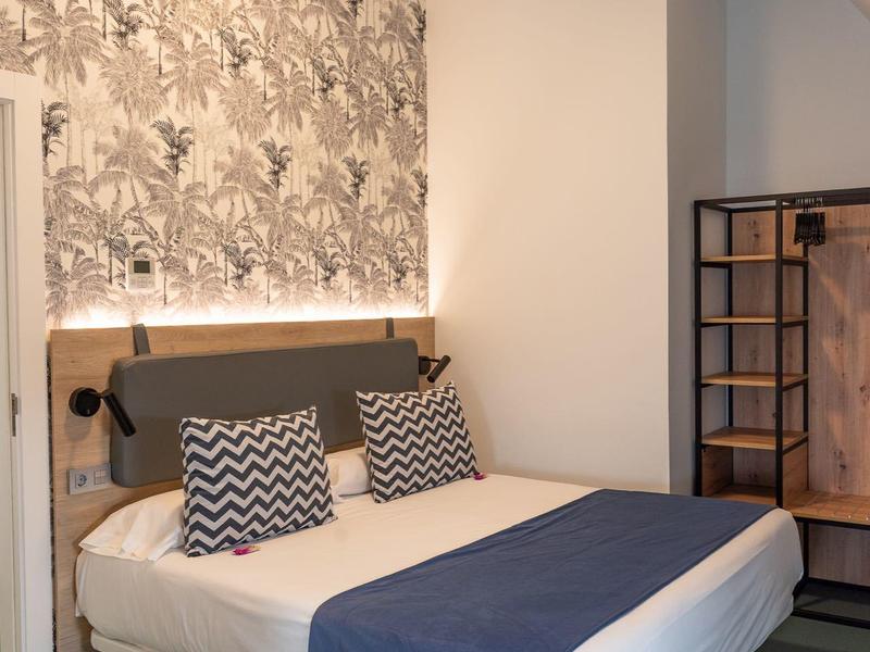 Camera d'hotel moderna con letto matrimoniale, cuscini a motivo e carta da parati elegante.