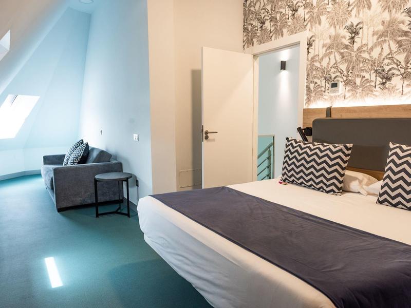 Camera moderna con letto matrimoniale, cuscini decorativi e divano vicino alla finestra.