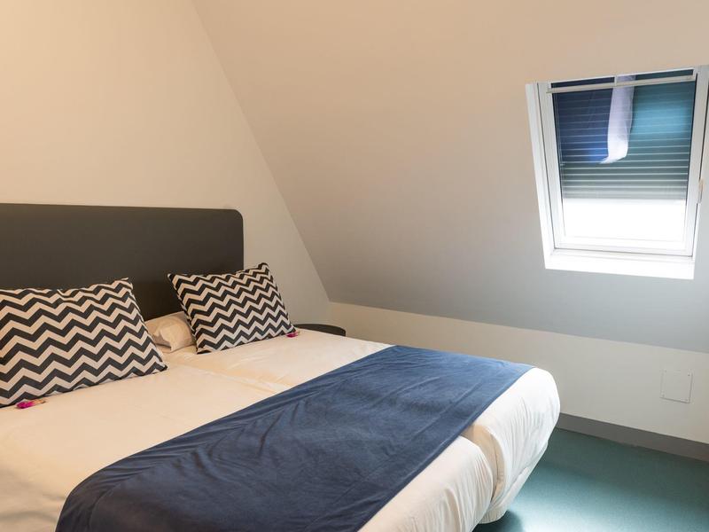 Piccola camera da letto con letto matrimoniale, cuscini a zigzag e finestra sul tetto con vista sul cielo.