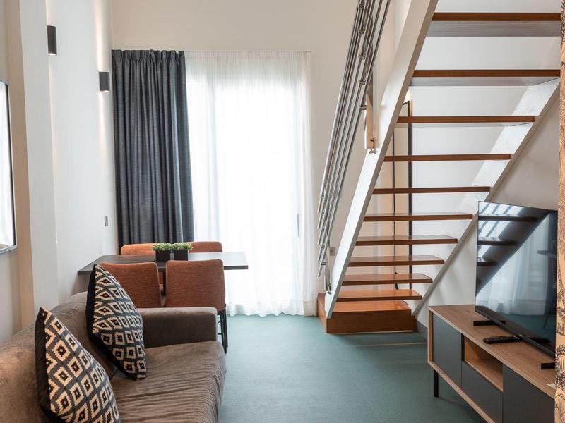 Soggiorno luminoso con divano, scala e grande finestra con tende.