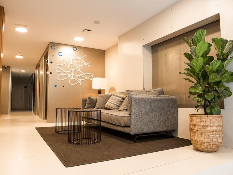 Area lounge moderna dell'hotel con divano grigio, tavolini e pianta in stanza luminosa.