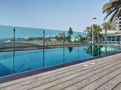 Infinity-Pool mit Holzdeck, Palmen und Meerblick unter klarem Himmel.