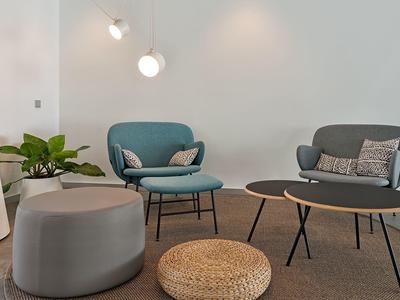 Moderner Sitzbereich mit blauem Sessel, grauem Sofa, Pouf und Pflanzen an weißer Wand.