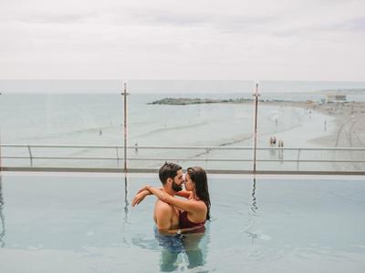Paar umarmt sich im Pool mit Blick auf das Meer und einen bewölkten Himmel im Hintergrund.