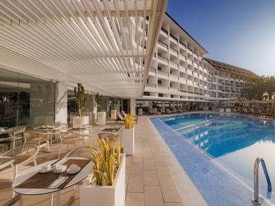 Piscina moderna de hotel con mobiliario de terraza y edificio de hotel de varios pisos a la luz del sol.