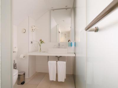 Baño moderno y luminoso con espejo grande, toallas blancas y diseño minimalista.