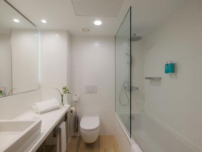 Baño moderno con bañera, inodoro, lavabo y gran espejo en colores neutros.