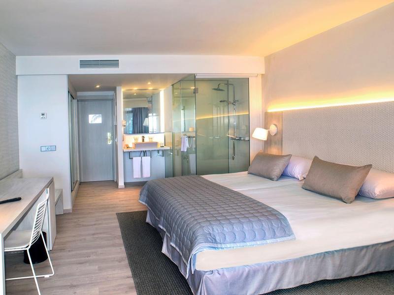 Modern hotel room with a bed, desk, chair, TV, and glass-walled bathroom.