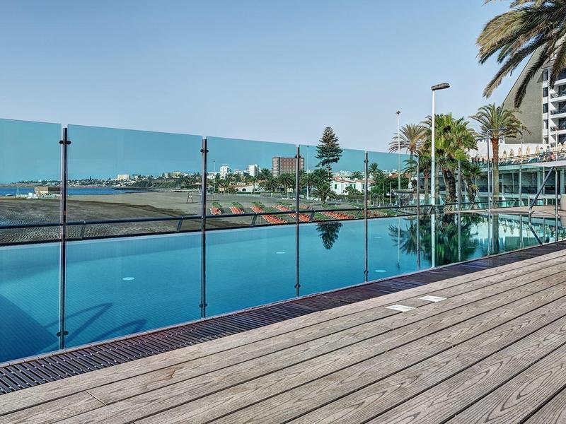 Infinity pool overlooking the ocean with wooden deck and palm trees nearby.