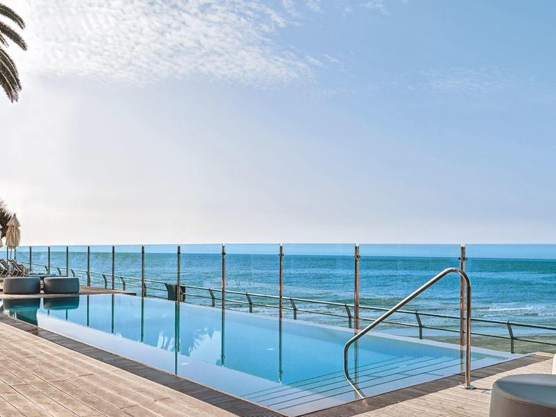 Infinity pool with ocean view and sun terrace under clear sky.