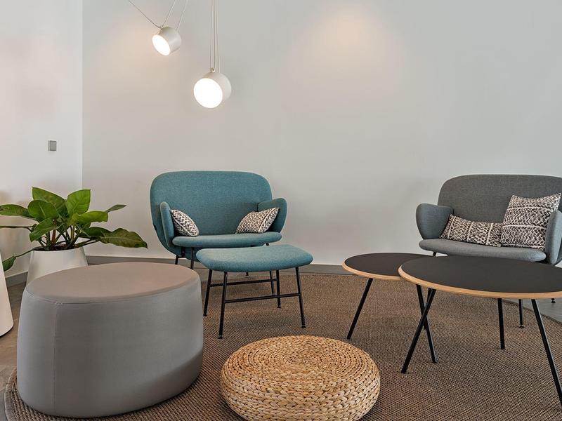 Modern seating area with blue chairs, round tables, and plants in a calm, minimalist space.