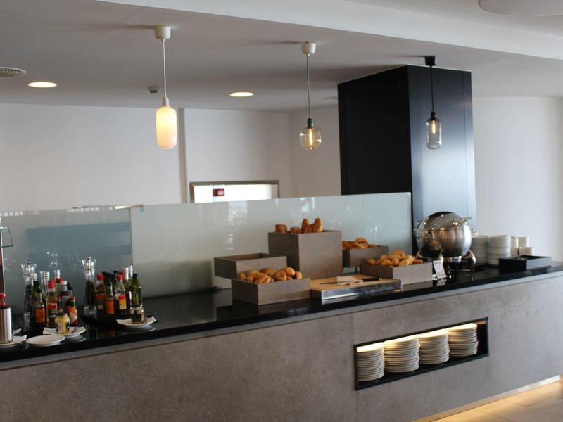 Modern hotel breakfast buffet with pastries, drinks, and warm lighting overhead.