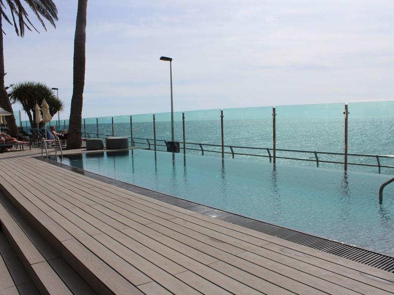 Infinity pool overlooking the sea with wooden deck and palm trees nearby.