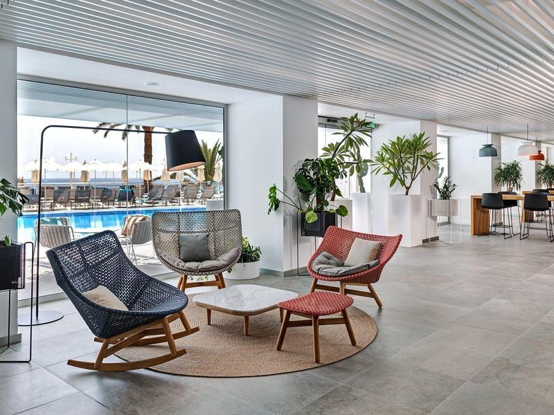 Modern hotel lobby with seating area, plants, and view of outdoor pool.