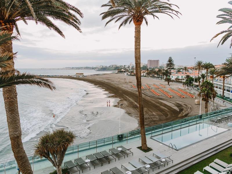 Beachside view with palm trees, a pool, and lounge chairs overlooking the ocean and coastline.