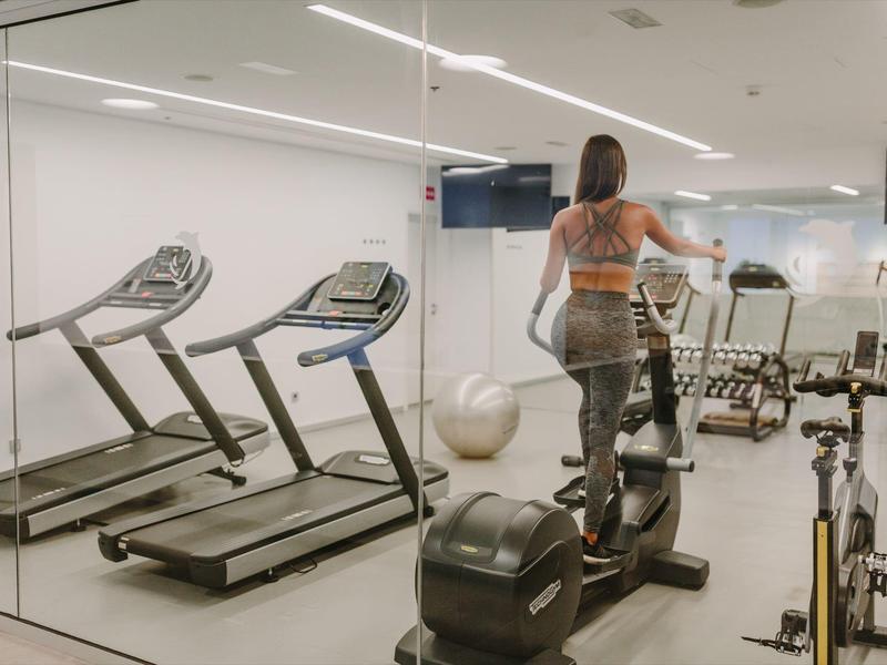 Modern gym with cardio machines, mirrored walls, and a person exercising inside a hotel fitness room.