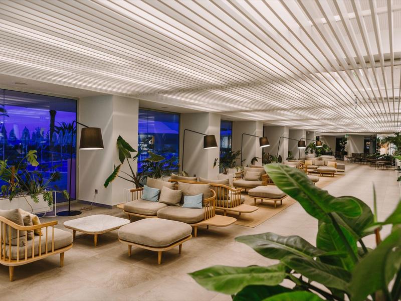 Spacious hotel lobby with modern seating, large windows, plants, and soft ambient lighting.