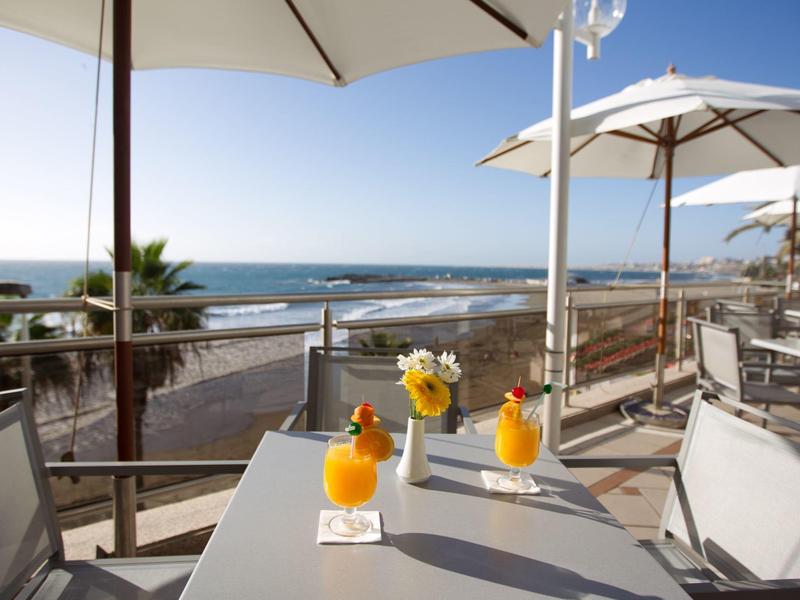 Outdoor table with drinks and flowers at a seaside terrace overlooking the ocean.