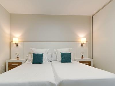 Modern hotel room with two single beds, white linens, green pillows, and bedside tables with lamps.