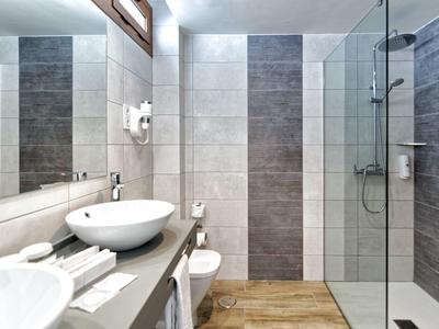 Modern bathroom with washbasin, mirror, and walk-in shower with glass partition.