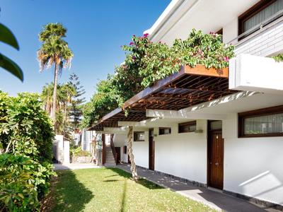 Modern holiday complex with white buildings, green plants, and palm trees in sunlight.