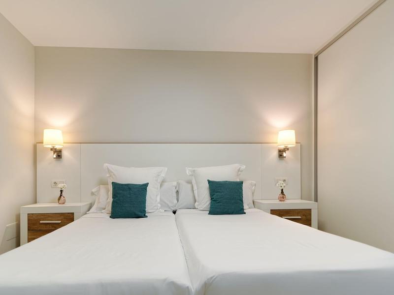 Modern hotel room with two single beds, white linens, green pillows, and bedside tables with lamps.