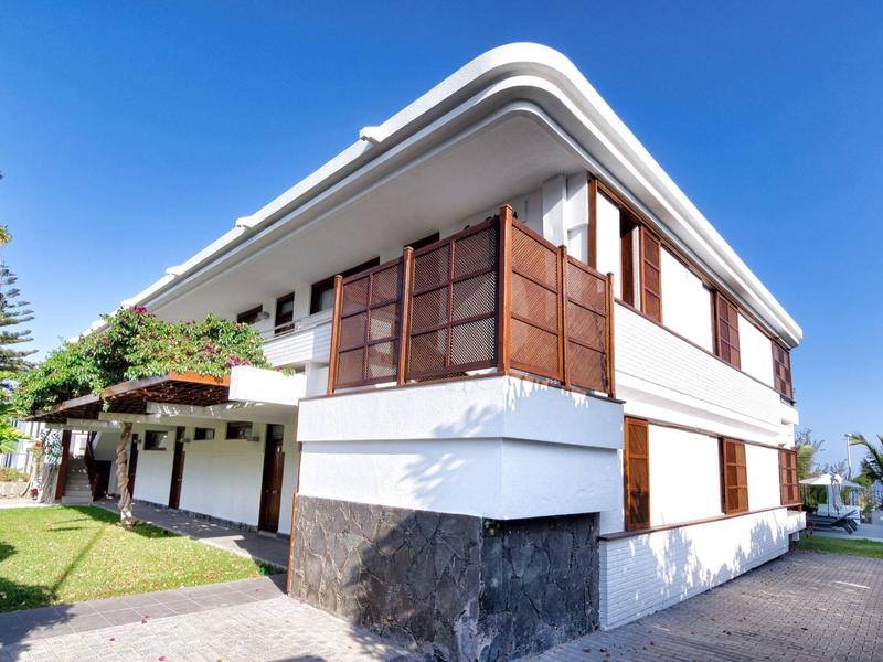 Modern white hotel building with large wooden windows and clear blue sky.