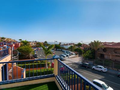 Vue depuis un balcon sur un parking et une rue par une journée ensoleillée dans un quartier résidentiel.