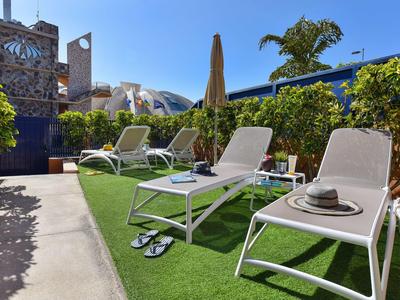 Terrasse avec chaises longues, parasol et vue sur des murs bleus et une horloge