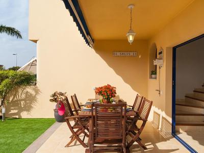 Terrasse couverte avec table en bois et six chaises à côté d'un jardin.