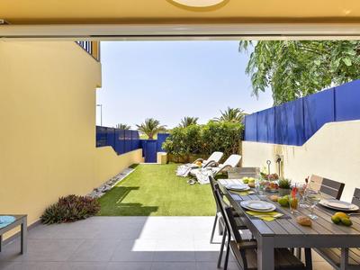 Terrasse avec table à manger et chaises longues sur pelouse, entourée de murs jaunes et bleus.