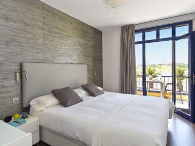 Chambre d'hôtel moderne avec lit double, mur d'accent gris et balcon avec vue.