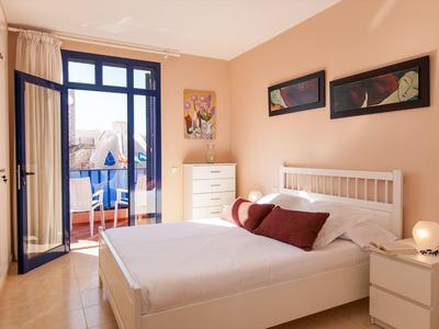 Chambre lumineuse avec lit double, meubles blancs et accès à un balcon donnant sur le quartier.