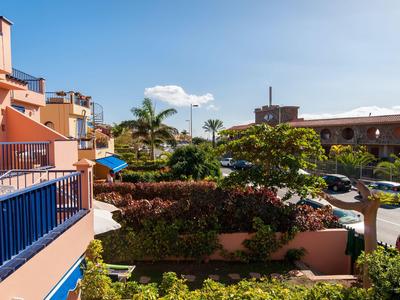 Widok z balkonu na parking i tropikalne rośliny pod niebieskim niebem.