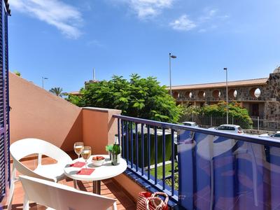 Petit balcon avec deux chaises, table, boissons et vue sur une rue calme.