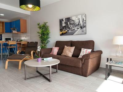 Salon confortable avec canapé marron, fauteuil, table basse et coin cuisine moderne.